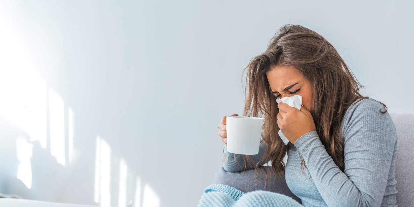 A young woman sneezes into a tissue